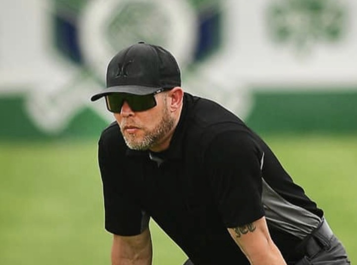 Baseball umpire in crouch position with sunglasses, preparing to call a play during a Missouri game